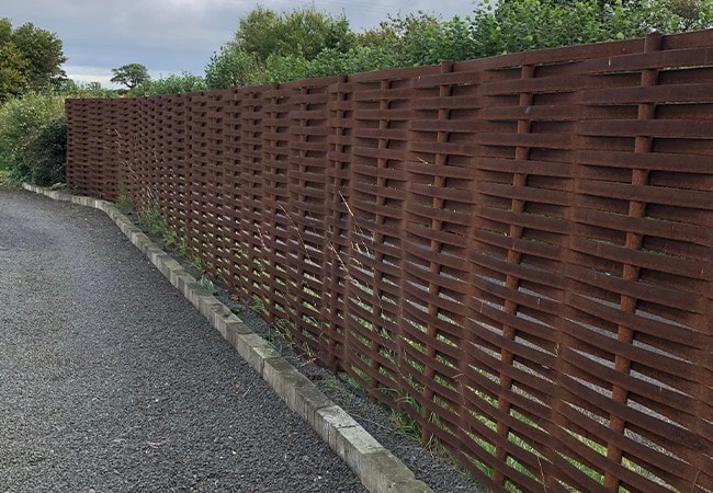 completed metal woven fence by a pavement.
