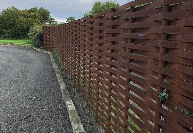 Complete, aged metal woven fence on gravel.
