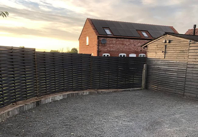 Complete black woven metal fence next to small wooden building.