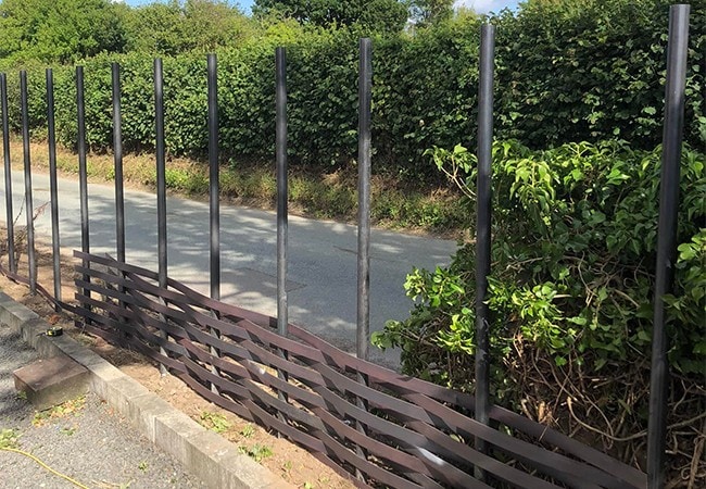 Metal being woven onto poles to create fence.