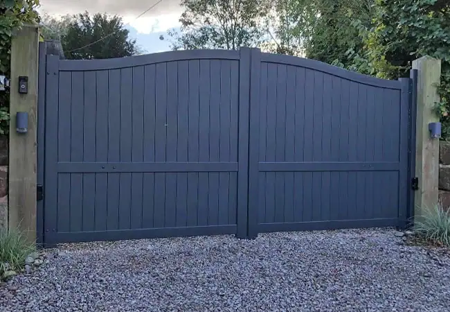 Tall grey wooden fence on gravel.