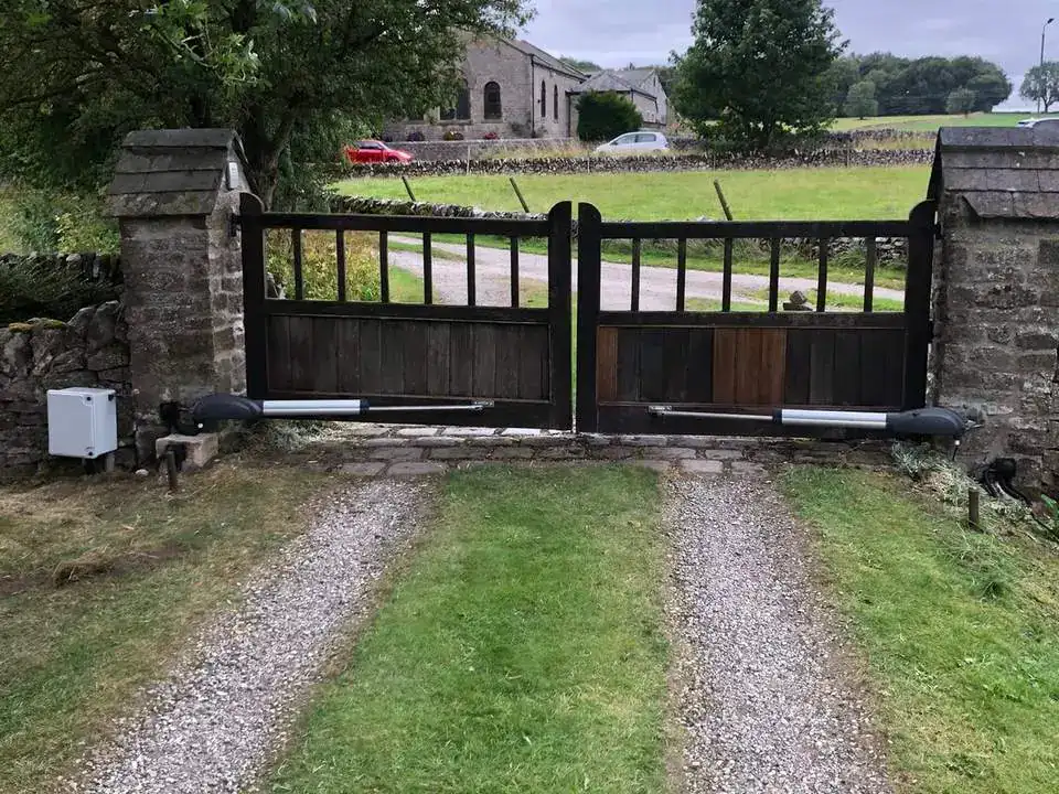 Timber-panelled gates between stone piers at the end of a grass-centred drive