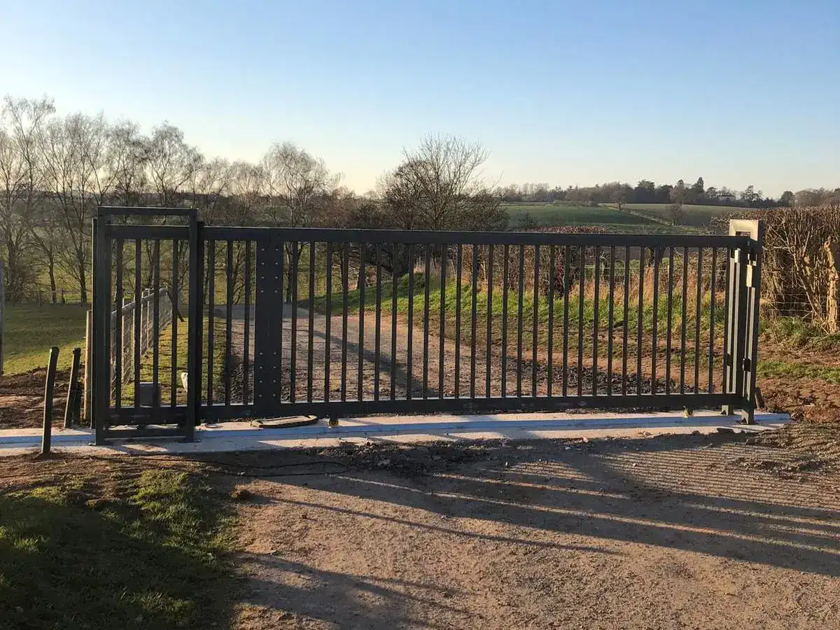 Steel sliding gate on a new concrete track across a farm entrance, fields behind
