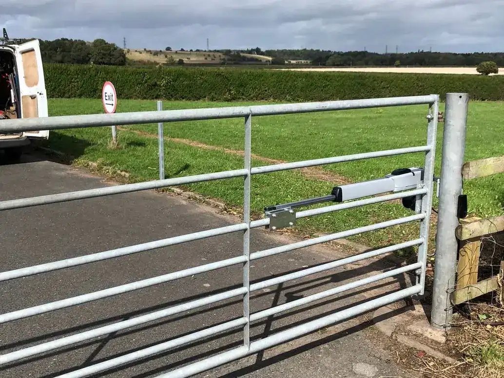 Galvanised field gate across a farm track beside a road, fields and hedgerows behind