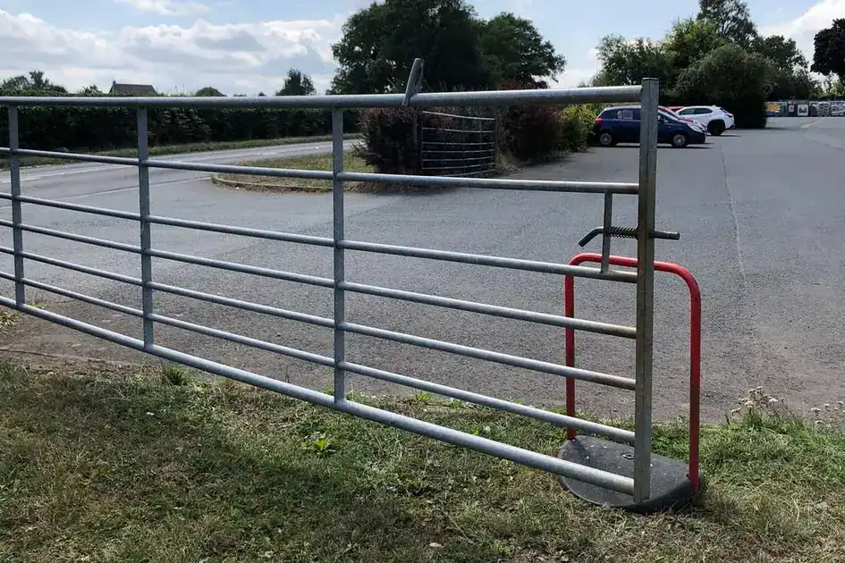 Wide galvanised field gate open across a farm entrance, a yard beyond
