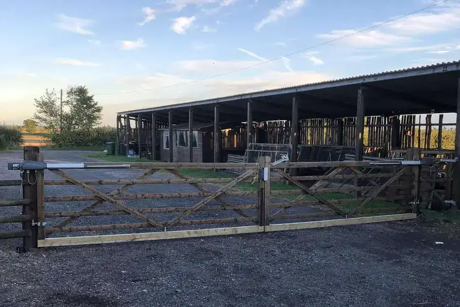 Timber five-bar gates with ram arms across a yard in front of an open-fronted barn