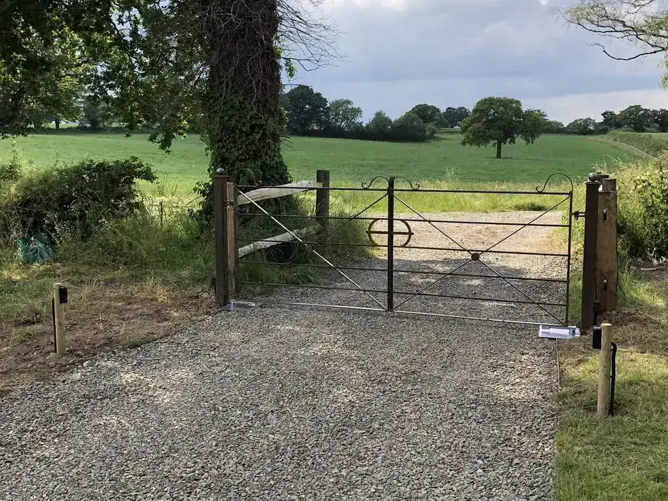 Iron estate gate at the end of a gravel drive under an oak, fields beyond