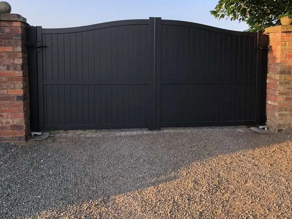 Anthracite solid-panel gates with an arched top between brick piers, gravel drive in front