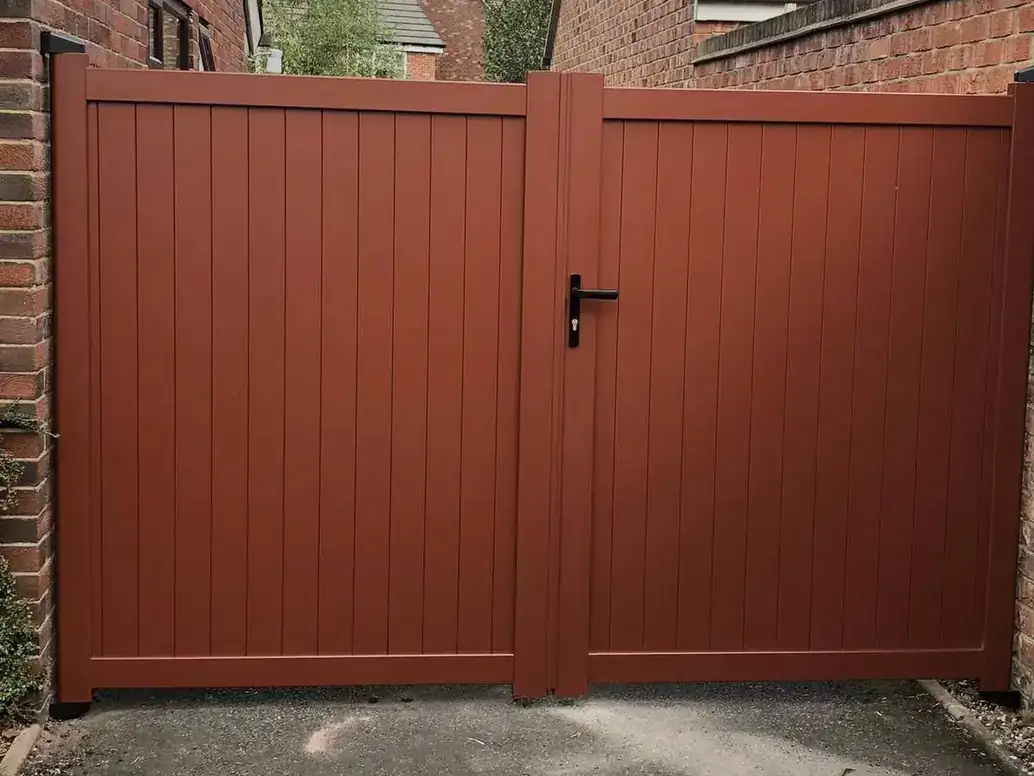 Red-brown solid-panel double gates with a pedestrian handle, between brick houses