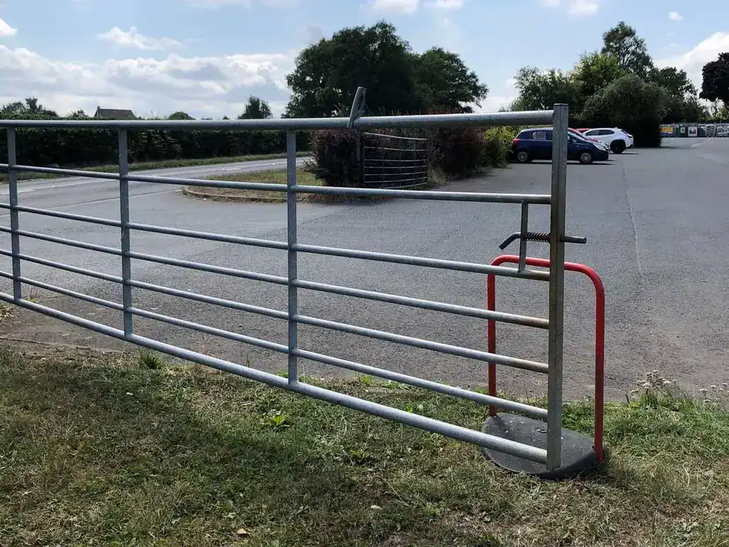 Wide galvanised field gate open across a farm entrance, a yard beyond