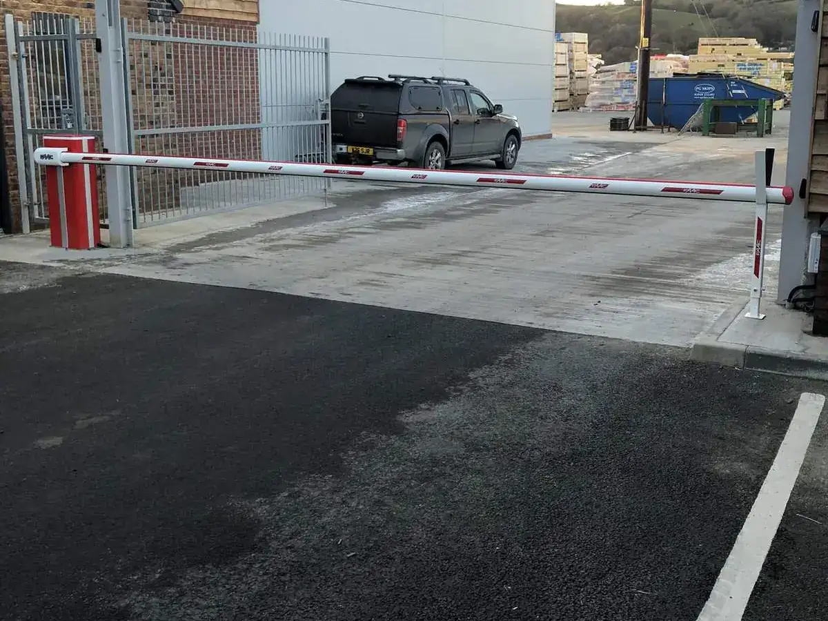 Red and white barrier arm across the entrance to a commercial yard beside a timber-clad building