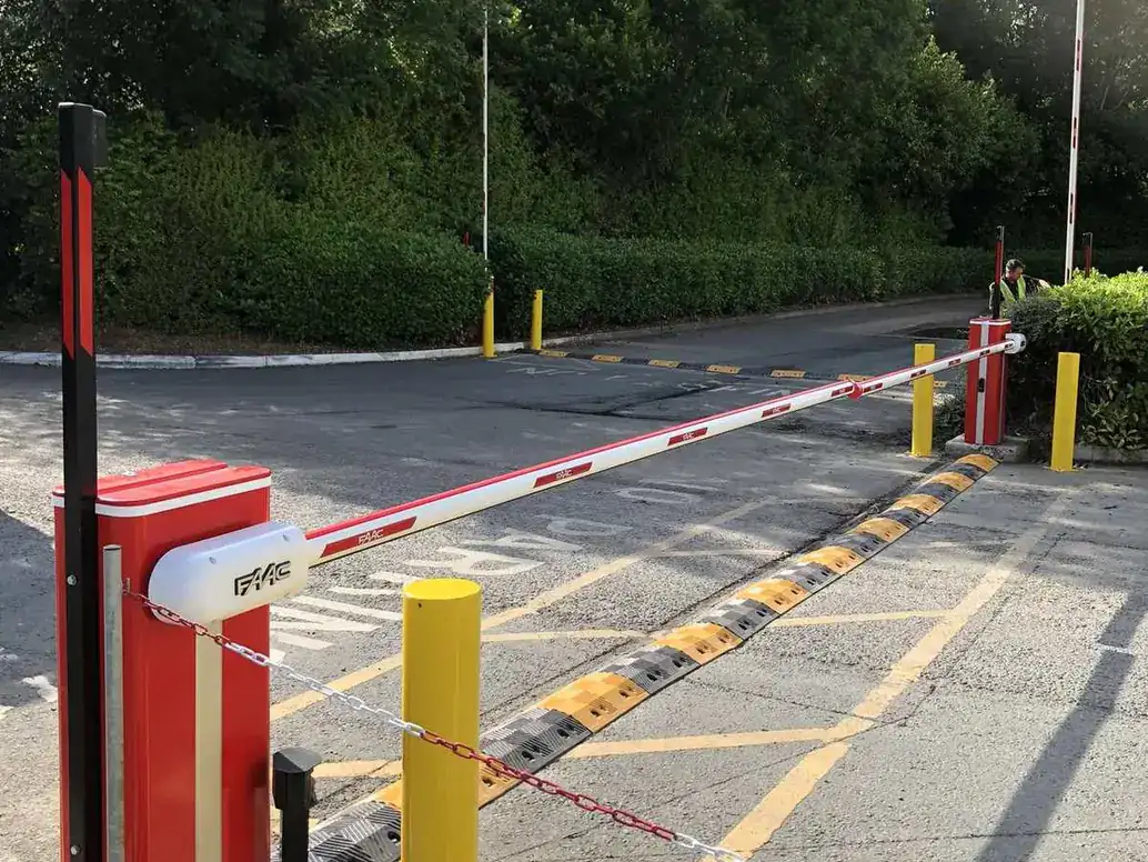 Yellow fixed bollards beside a red barrier and a speed bump at a car park entrance