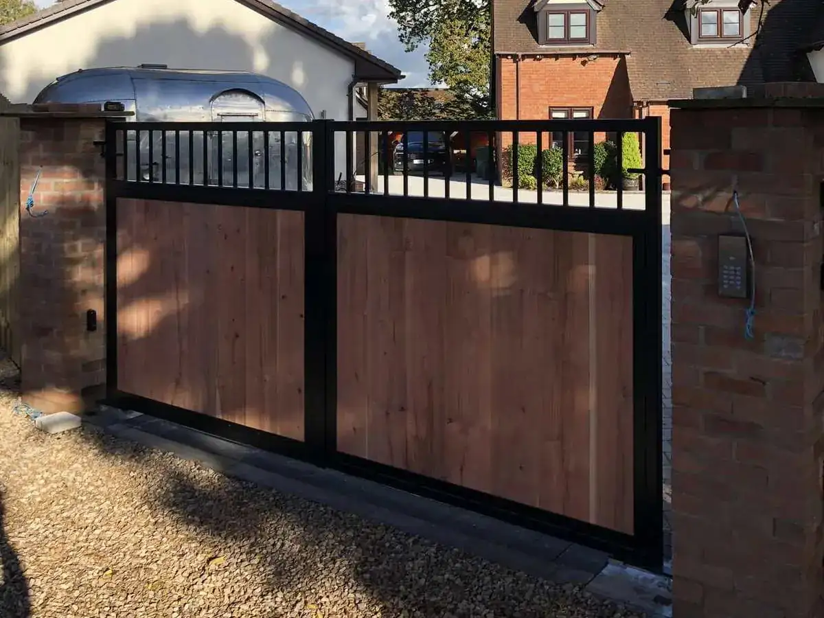 Black-framed timber driveway gates between brick piers, houses behind