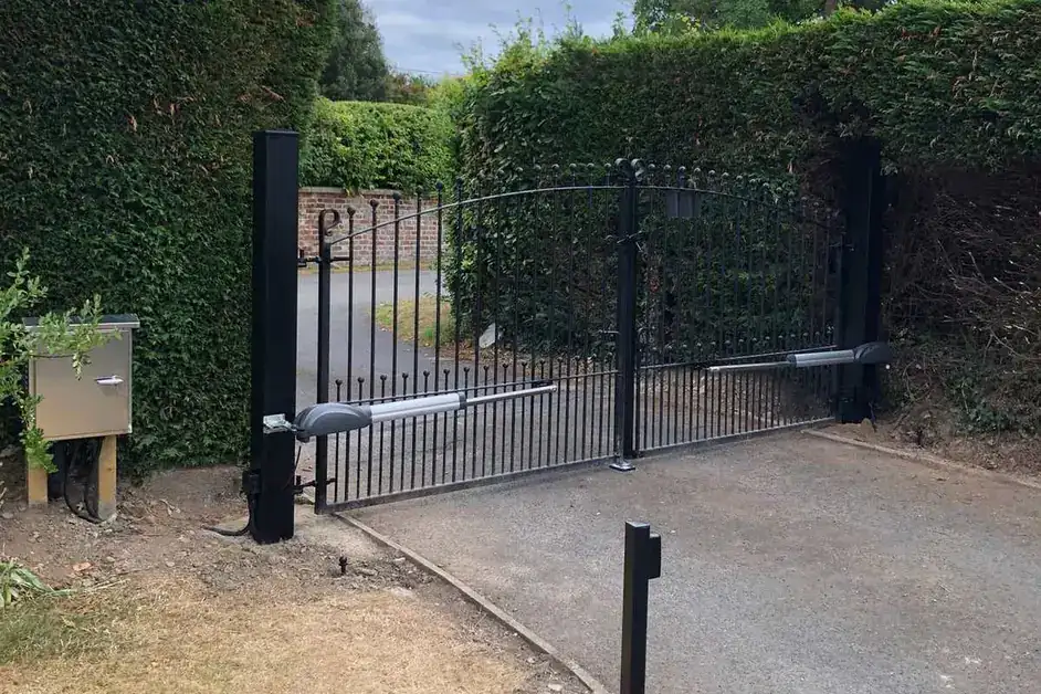 Automated iron gates between hedges, with a photocell post beside the drive