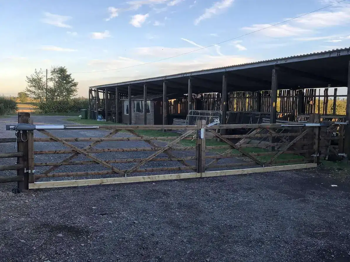 Timber five-bar gates across a yard in front of an open-fronted barn