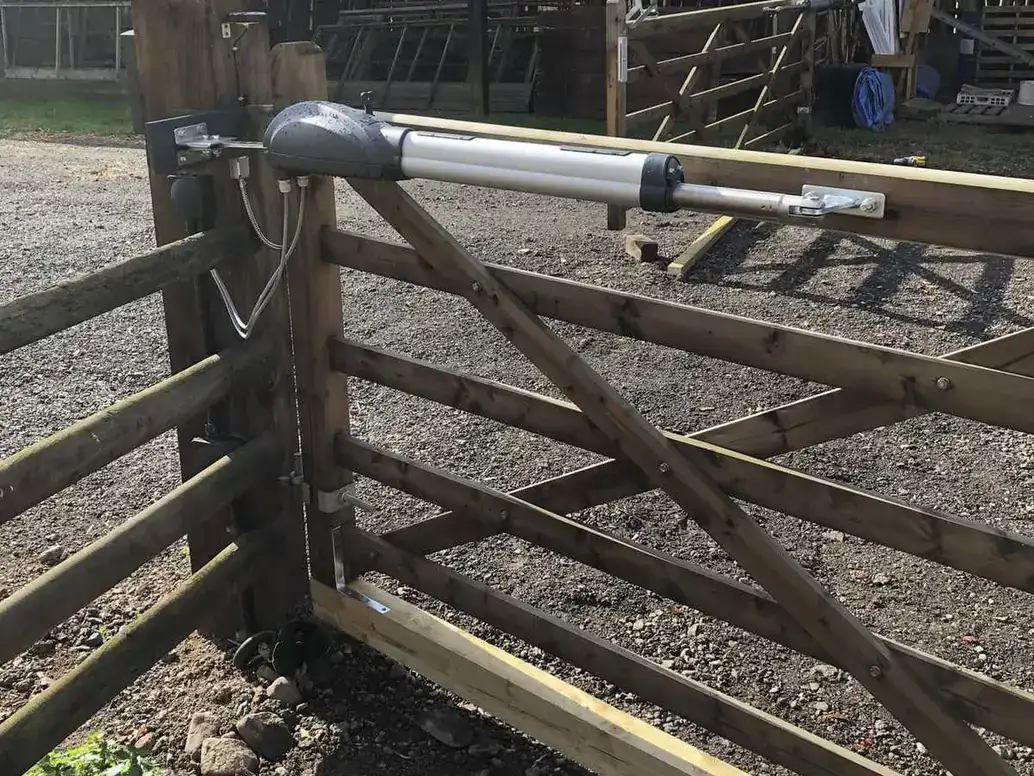 Timber gate with a ram arm across a yard beside a row of timber stables
