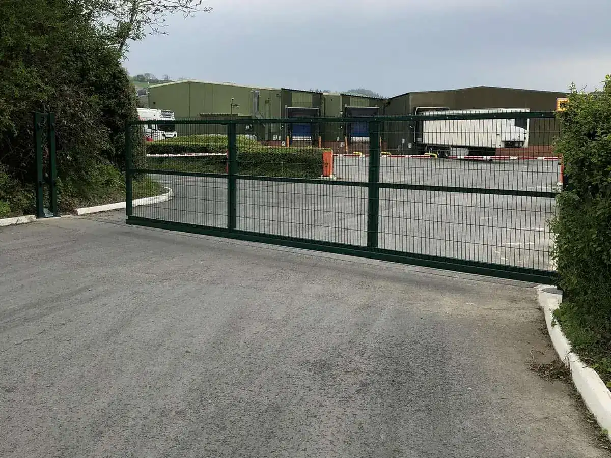 Green steel mesh sliding gate across the road into a commercial site