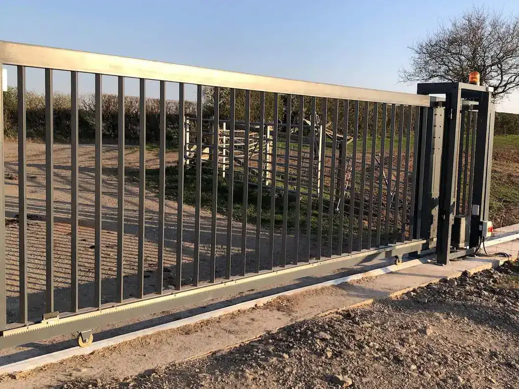 Steel sliding gate on a concrete track at a rural entrance, fields behind