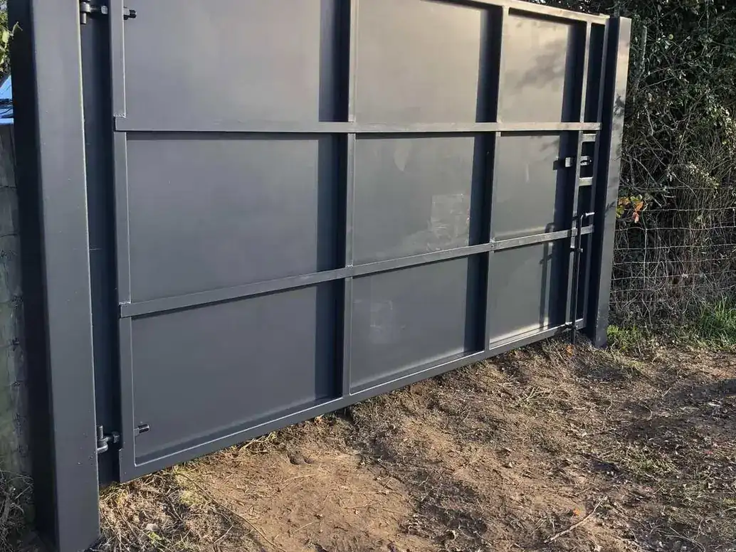 Large dark grey solid steel gate on a framed post beside a hedge