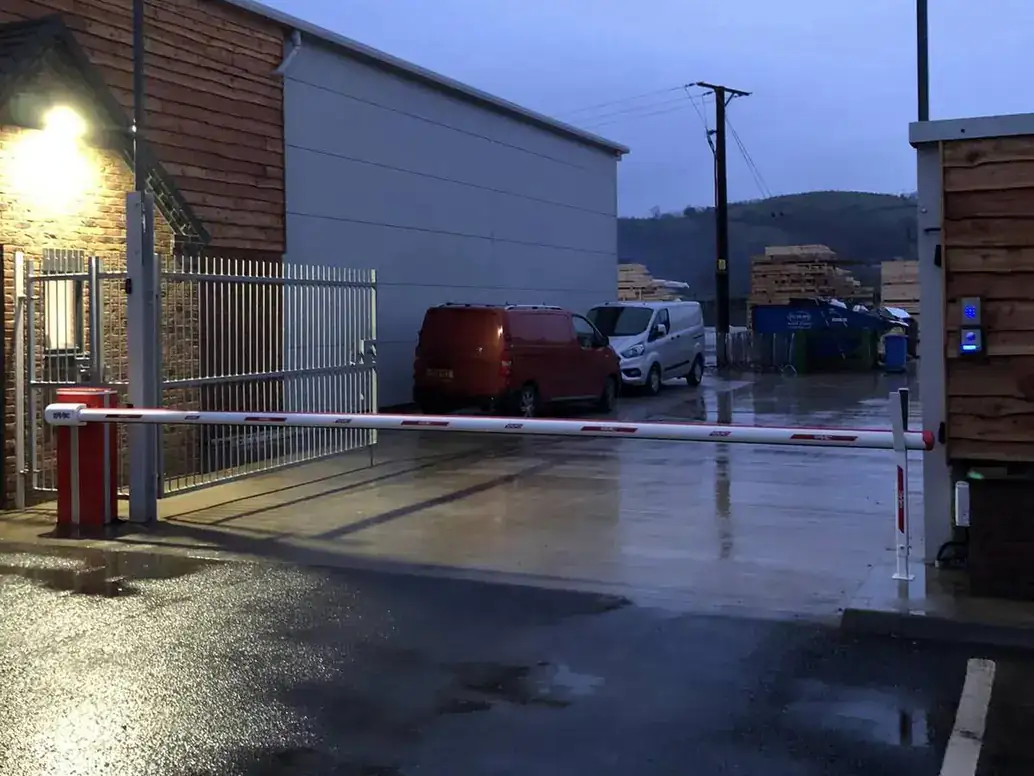 Red and white barrier across a commercial yard entrance at dusk, security light on