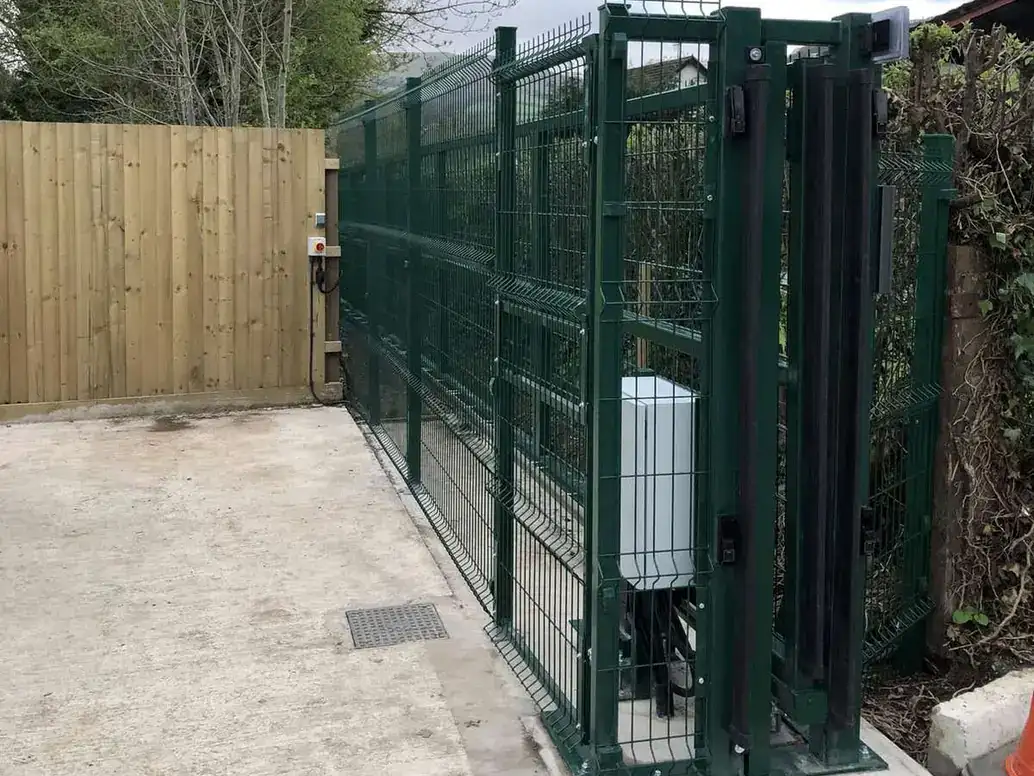 Motor housing at the foot of a green steel mesh sliding gate on a concrete base