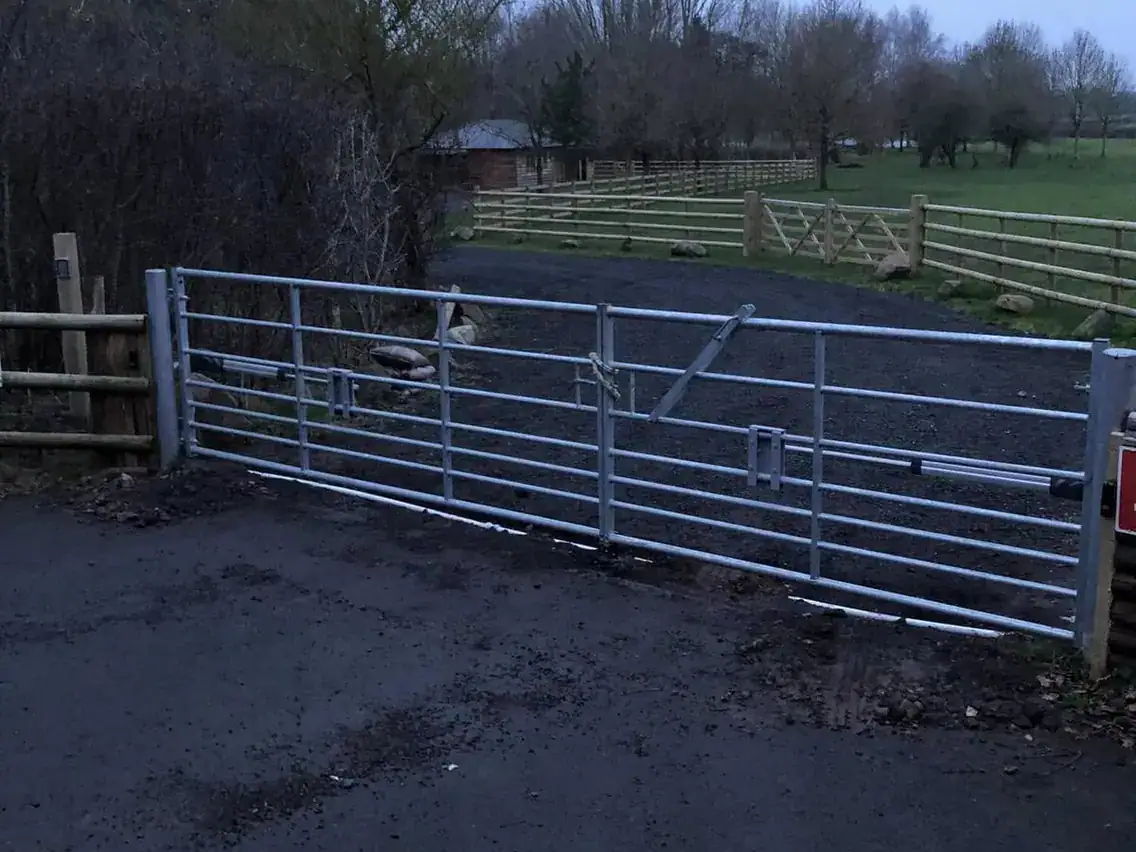 Galvanised field gate on timber posts across a farm entrance, post-and-rail fencing beyond