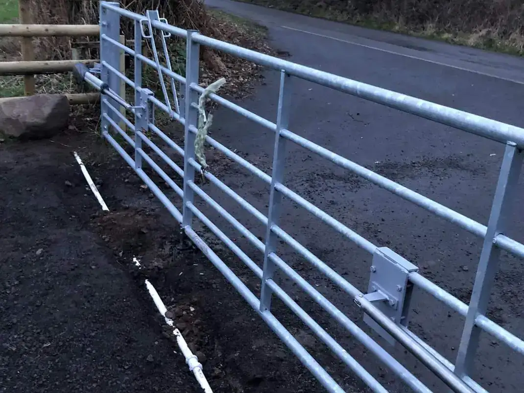 Long galvanised field gate on a timber post beside a lane