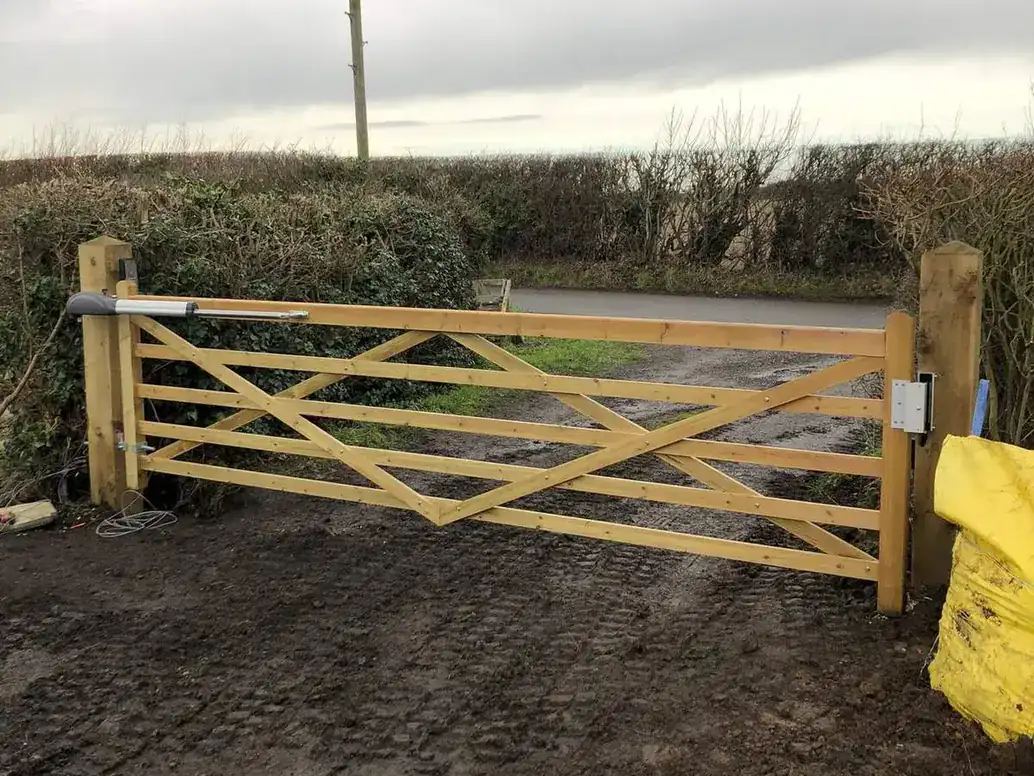 New timber five-bar gate hung between timber posts across a muddy farm entrance
