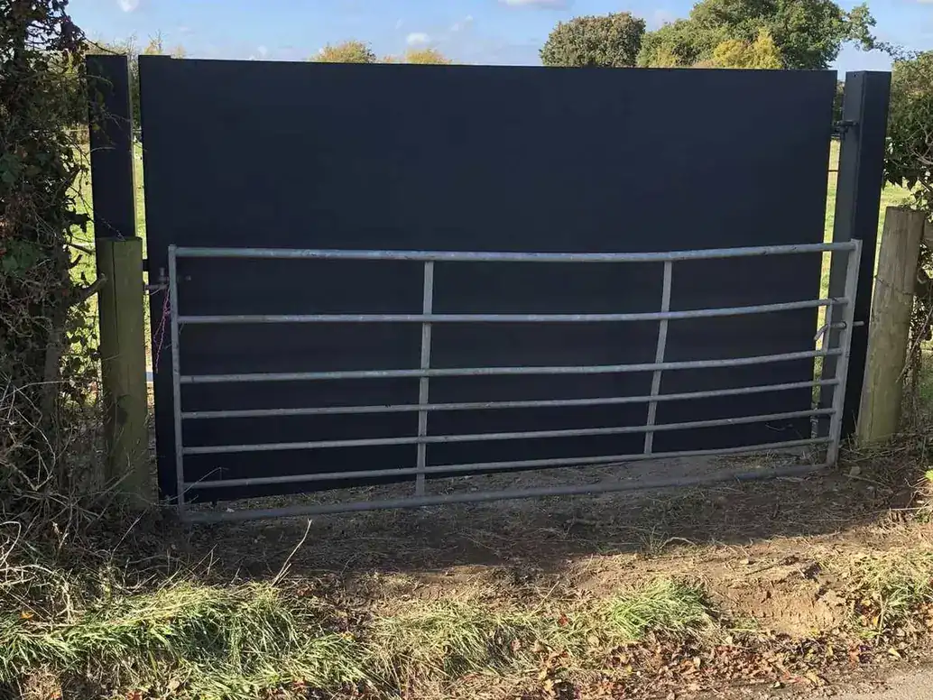 Galvanised field gate with a dark sheeted panel above it, blocking the view through a field entrance