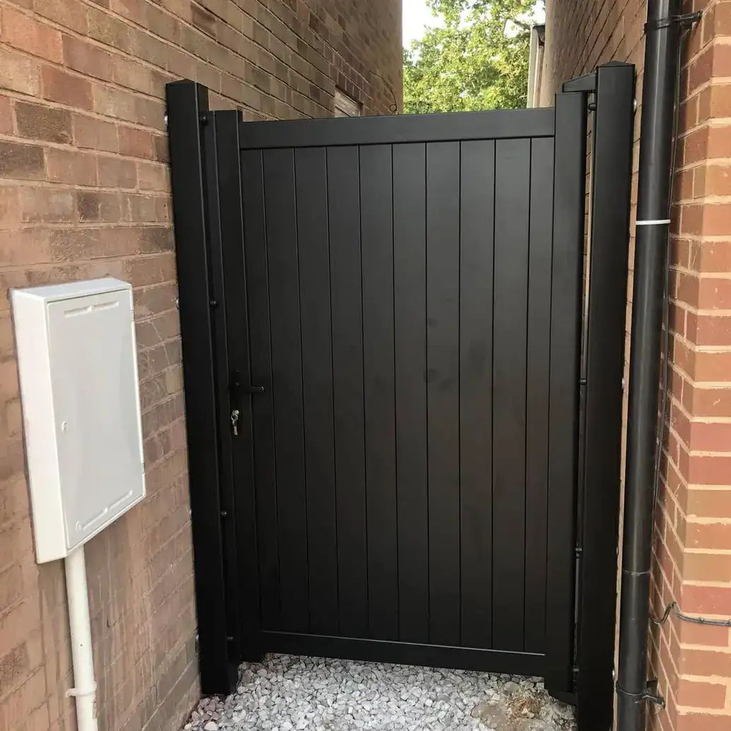 Tall black solid side gate closing a passage between two brick walls