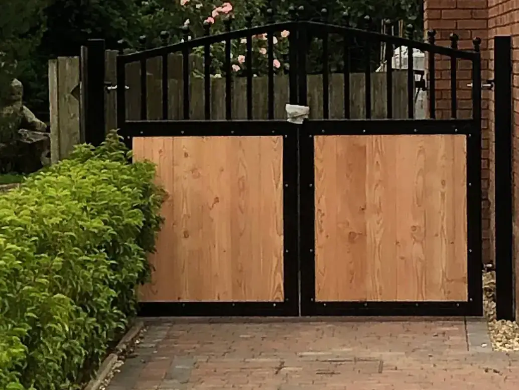 Black-framed garden gates with timber panels and an arched railing top, flowers either side