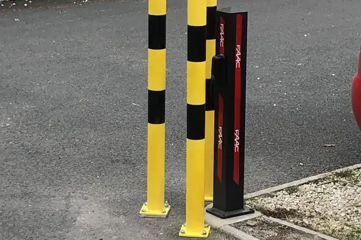 Red and black gate column behind yellow and black guard rails beside a tarmac drive