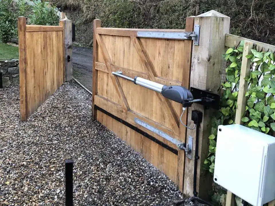 Oak gates with ram arms, a control cabinet and a photocell post on a gravel drive