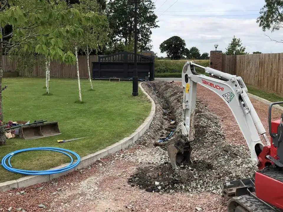 Mini digger trenching along a driveway during a gate installation
