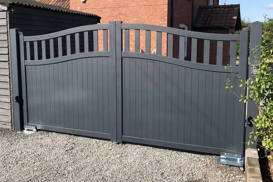Grey arched aluminium driveway gates in front of a red brick house