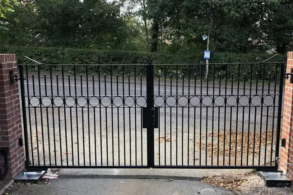 Black iron driveway gates with a band of ring detailing, between brick piers