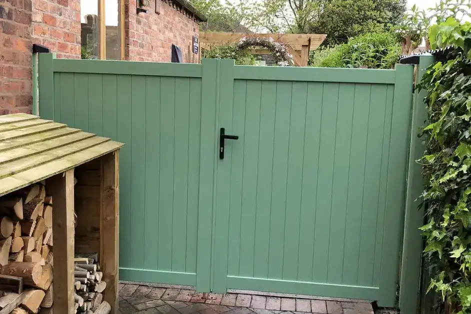Sage green garden gates beside a log store