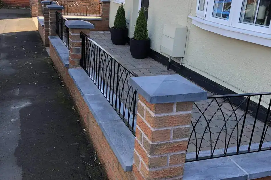 Black wall-top railings on a brick wall in front of a cream house