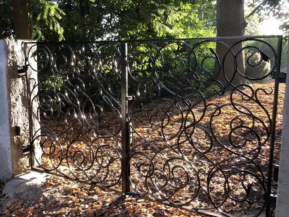 Bespoke scrollwork iron gates between white piers in autumn