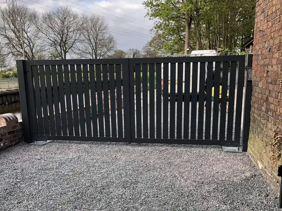 Dark grey aluminium swing gates across a gravel drive beside a brick house