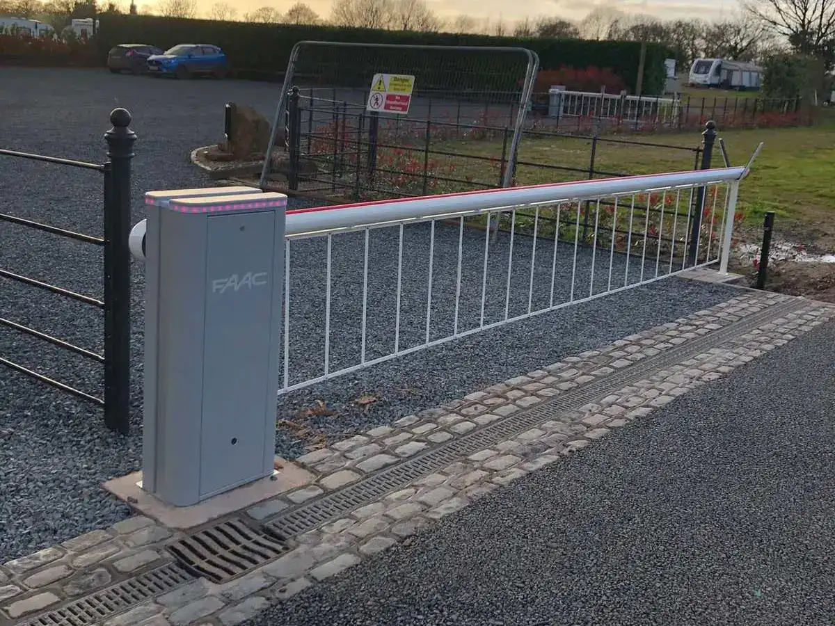 White barrier arm with a hanging skirt across a new gravel entrance at sunset