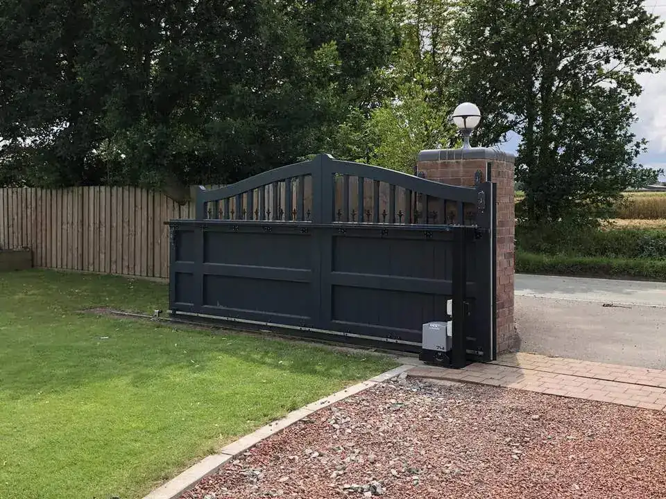 Black solid-panel gates at the end of a red gravel drive, lawn and trees either side