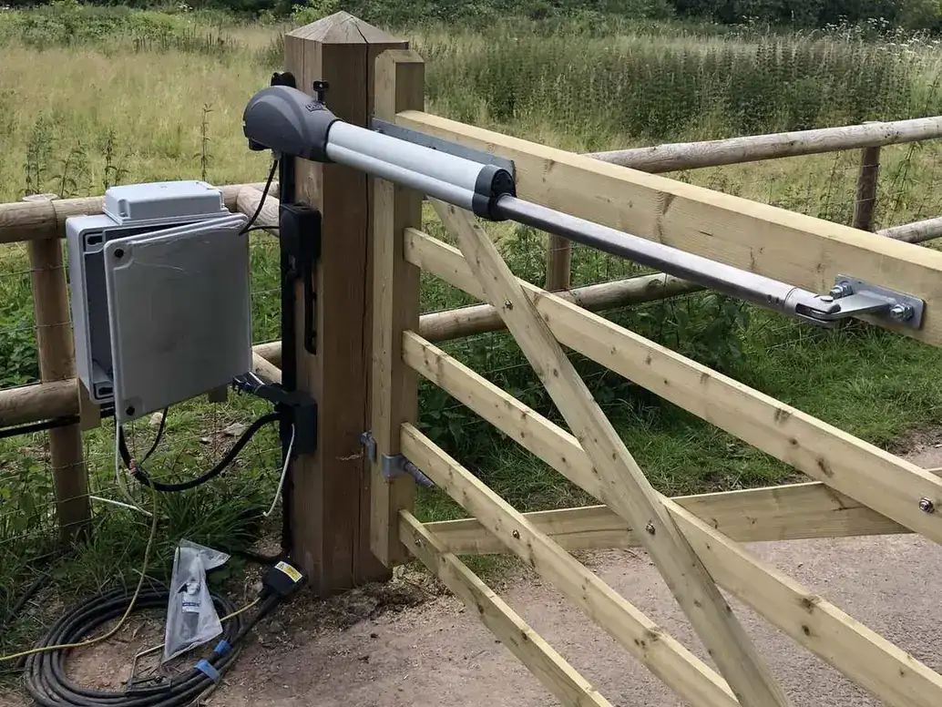 Ram arm and open control box on a timber five-bar gate, cabling being connected