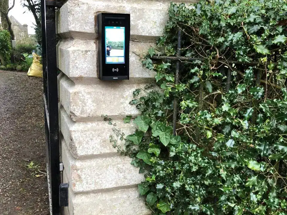 Video intercom on a stone gate pillar under a house-name plaque, beside an iron gate
