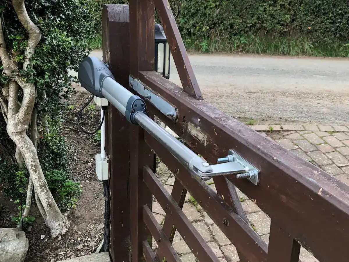 Ram arm fitted to a dark-stained timber five-bar gate beside a white house
