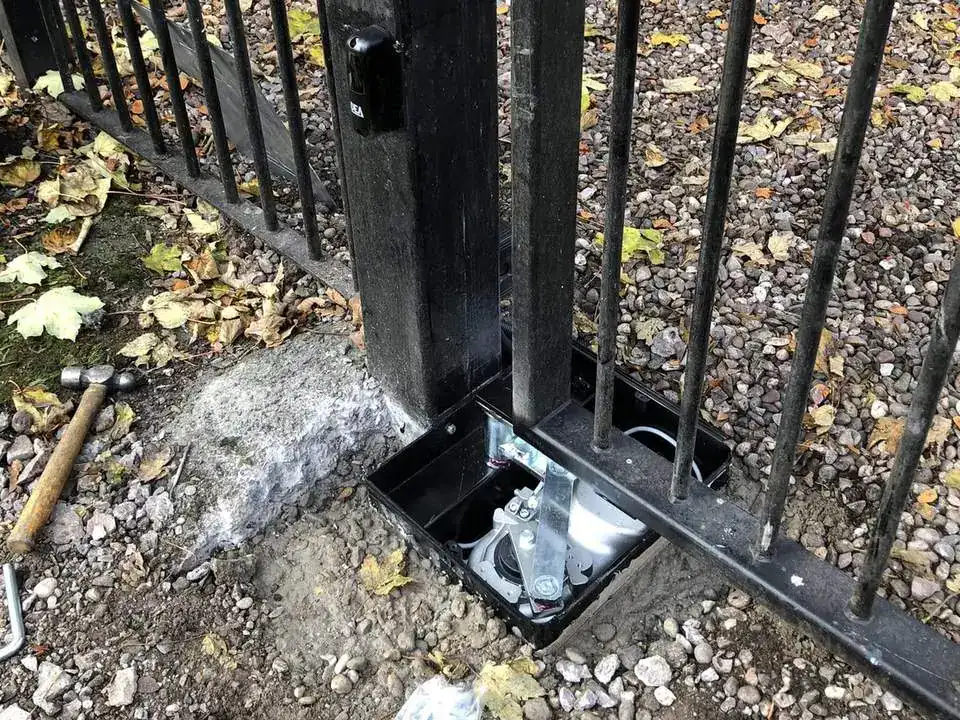 Iron gate post with the open foundation box of an underground operator at its foot