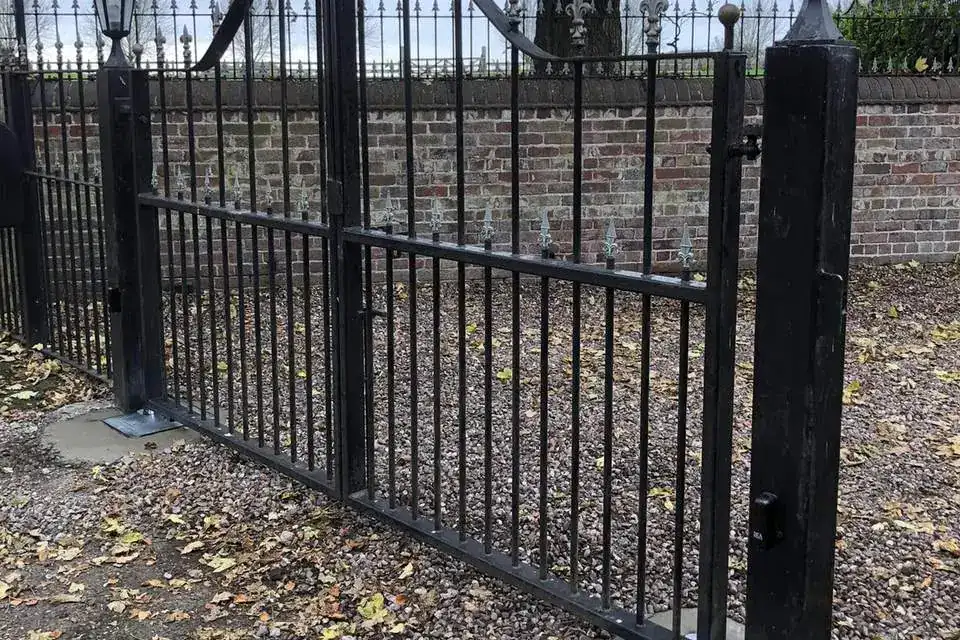 Black steel gate on a gravel drive beside a lamp post