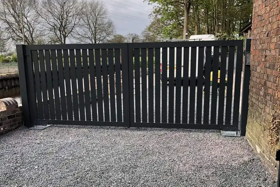 Dark grey aluminium swing gates across a gravel drive beside a brick house