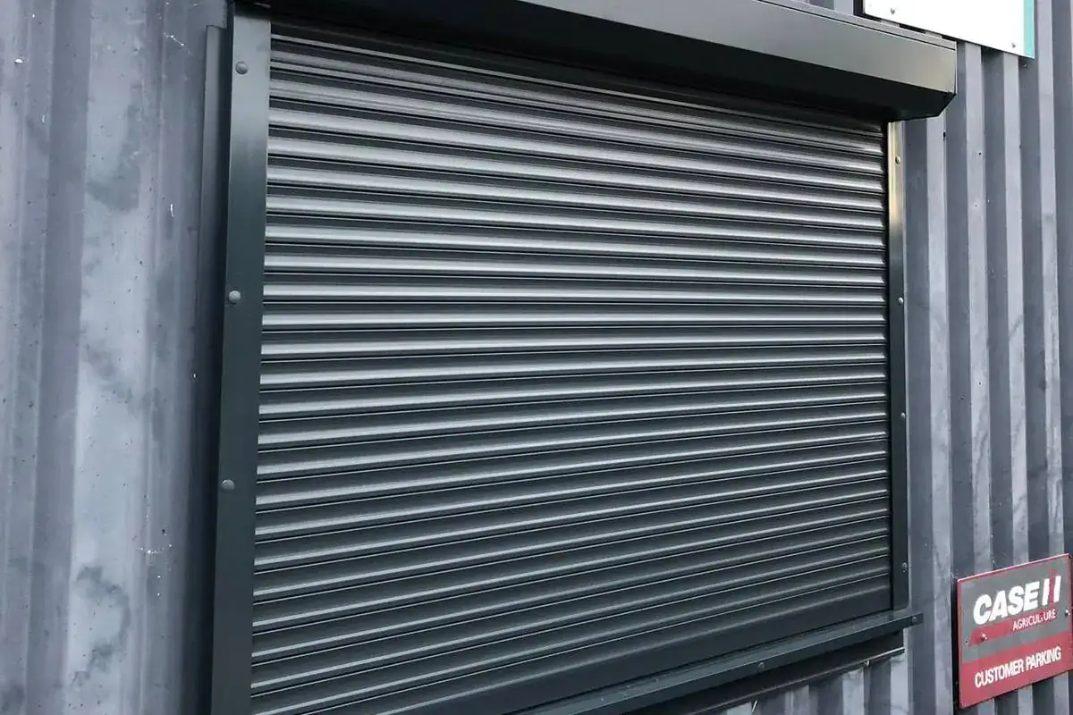Dark grey roller shutter over a window on a corrugated steel building