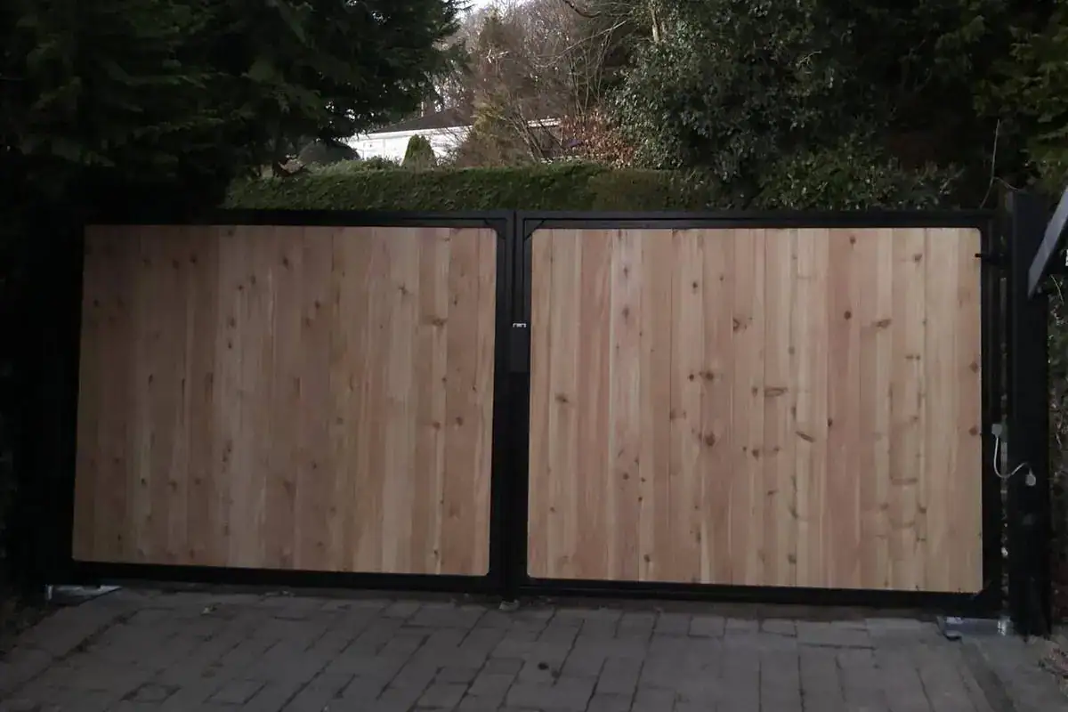 Cedar-clad gates in black steel frames across a block-paved drive
